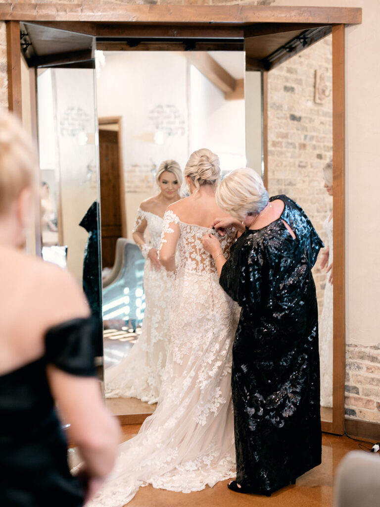 bride and mom buttoning her dress  | Chandelier of Gruene Wedding | Modern Black and White Chic Wedding | 