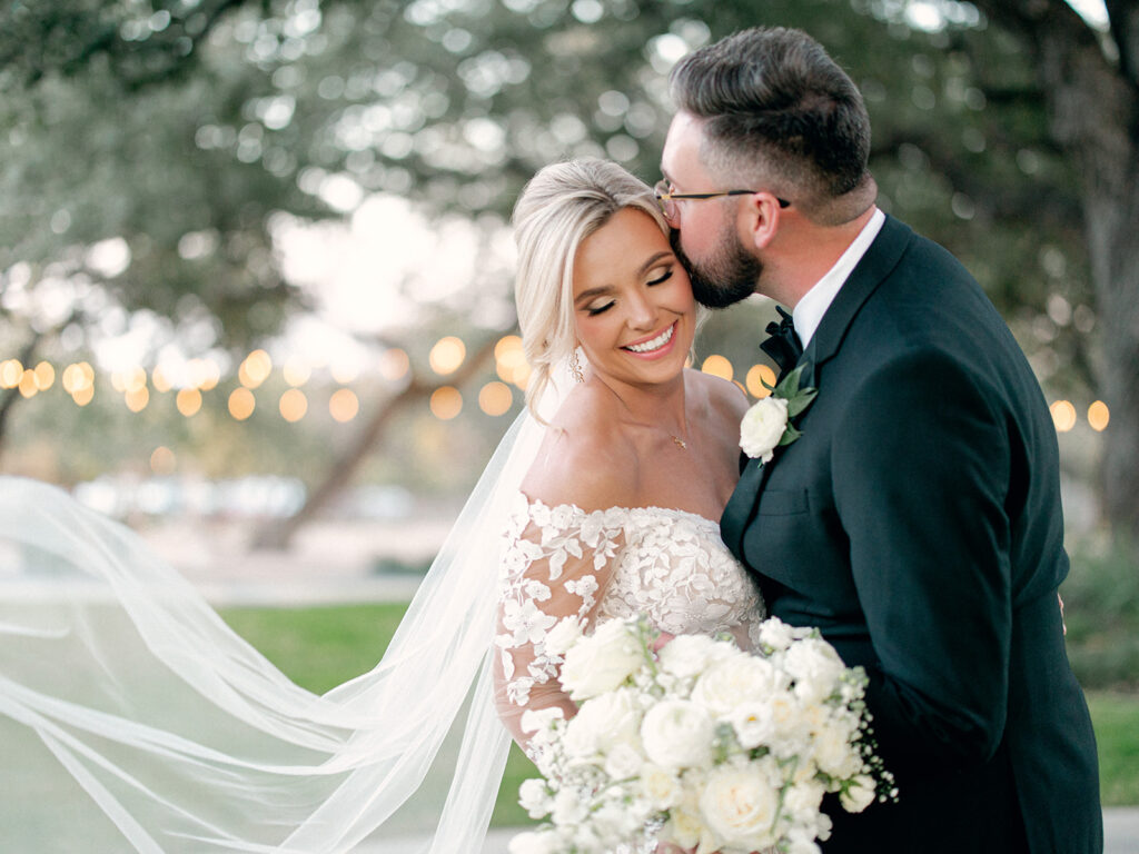 groom kissing bride on cheek | Chandelier of Gruene Wedding | Modern Black and White Chic Wedding | 