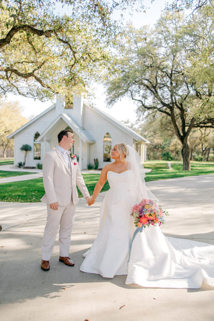 bride and groom in front of white chapel