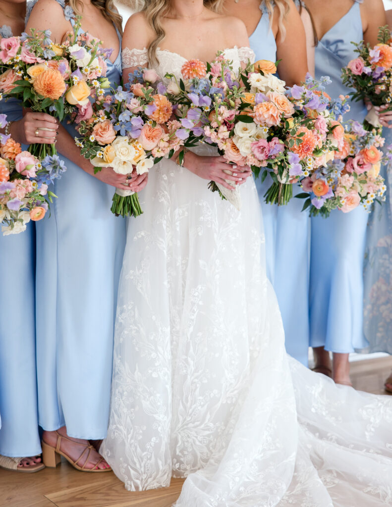 Bridesmaids holding pastel bouquets with peach, lavender, and blush blooms to accent light blue dresses

