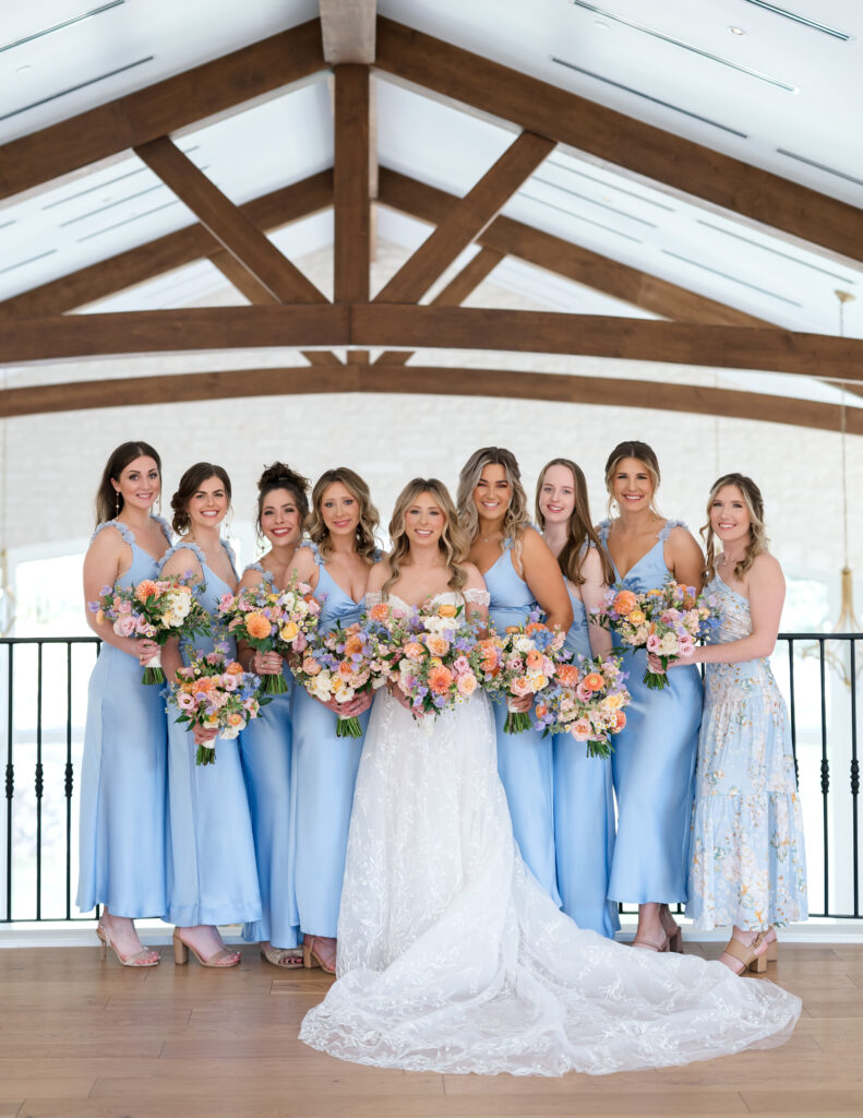 Bridesmaids holding pastel bouquets with peach, lavender, and blush blooms to accent light blue dresses