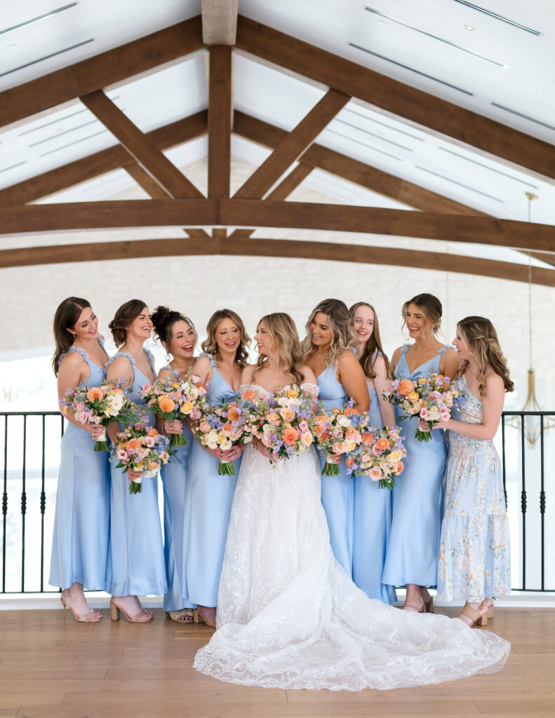 Bridesmaids holding pastel bouquets with peach, lavender, and blush blooms to accent light blue dresses