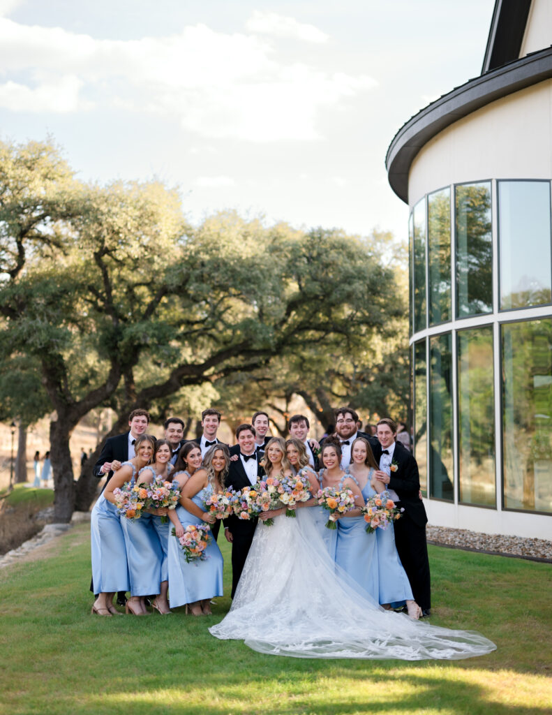 Kinsey and Colton walking with their bridal party at The Preserve at Canyon Lake surrounded by soft pastel blooms and blue bridesmaid dresses