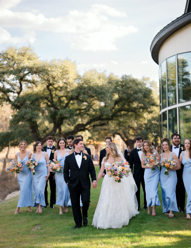 Kinsey and Colton walking with their bridal party at The Preserve at Canyon Lake surrounded by soft pastel blooms and blue bridesmaid dresses