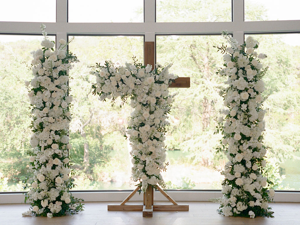 A duo of lush pillars of wedding day flowers accented the cross beautifully at this indoor ceremony
